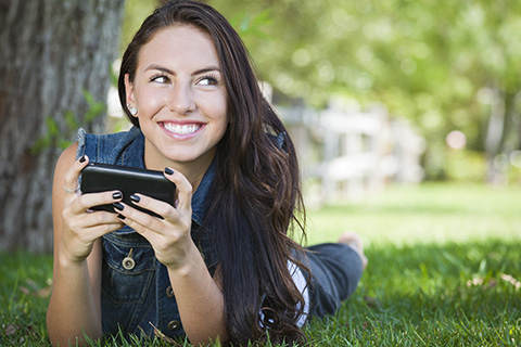 Attractive Happy Mixed Race Young Female Texting on Her Cell Phone Outside Laying in the Grass.